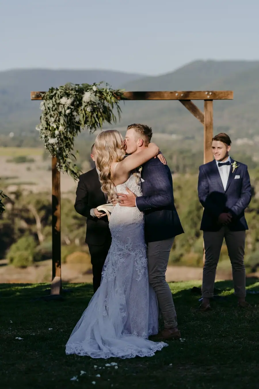 Newlyweds kissing beneath a wooden arch overlooking the valley