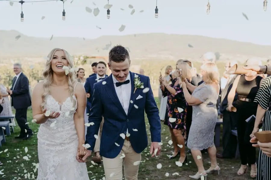 Newlyweds walking beneath falling petals as guests applaud