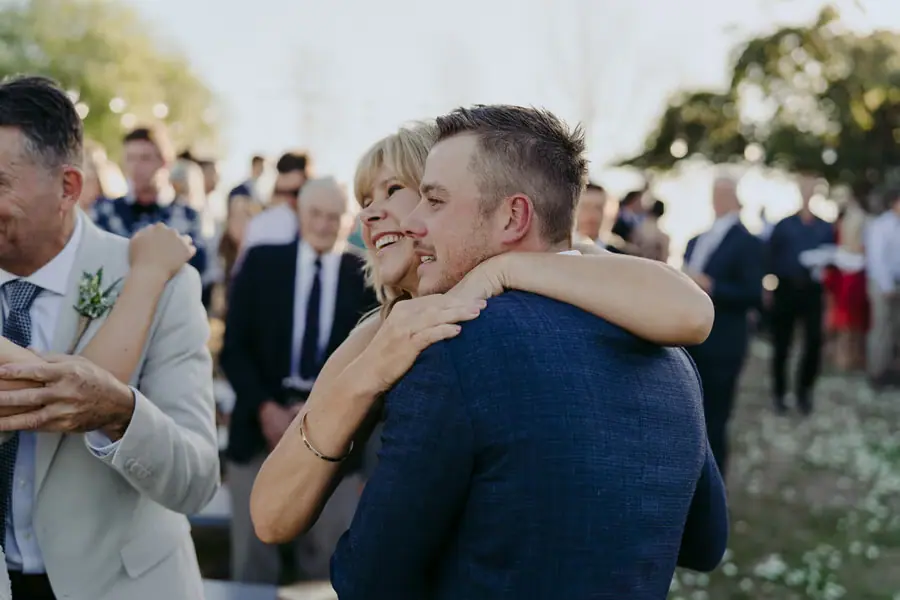 Groom smiling as a guest embraces him after the ceremony