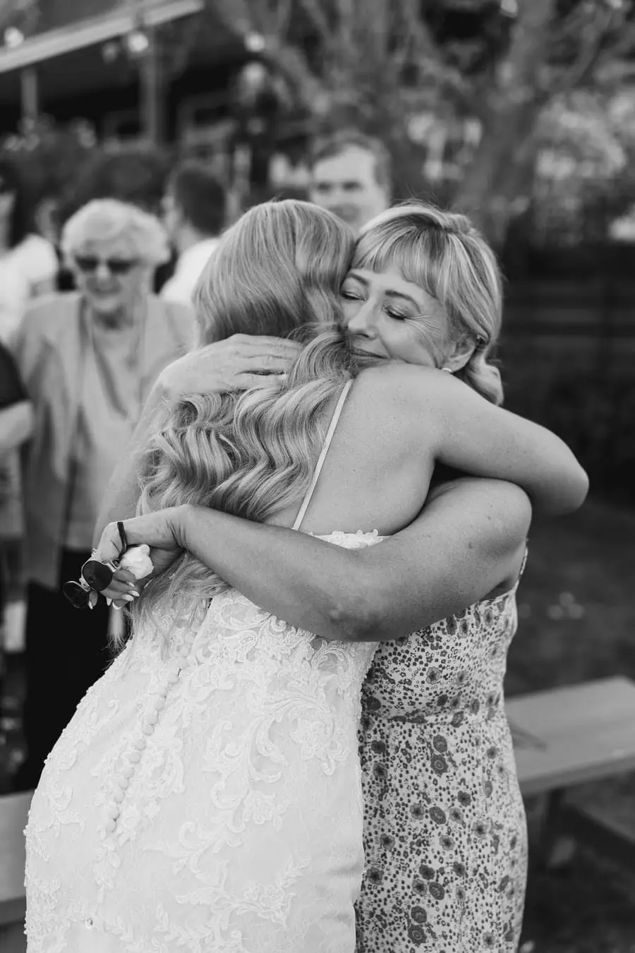 Black-and-white photograph of the bride hugging a guest wearing glasses
