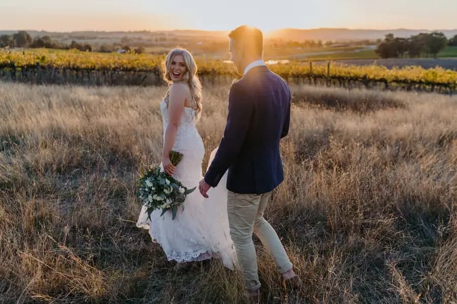 Bride looking back as she walks hand in hand with the groom at sunset