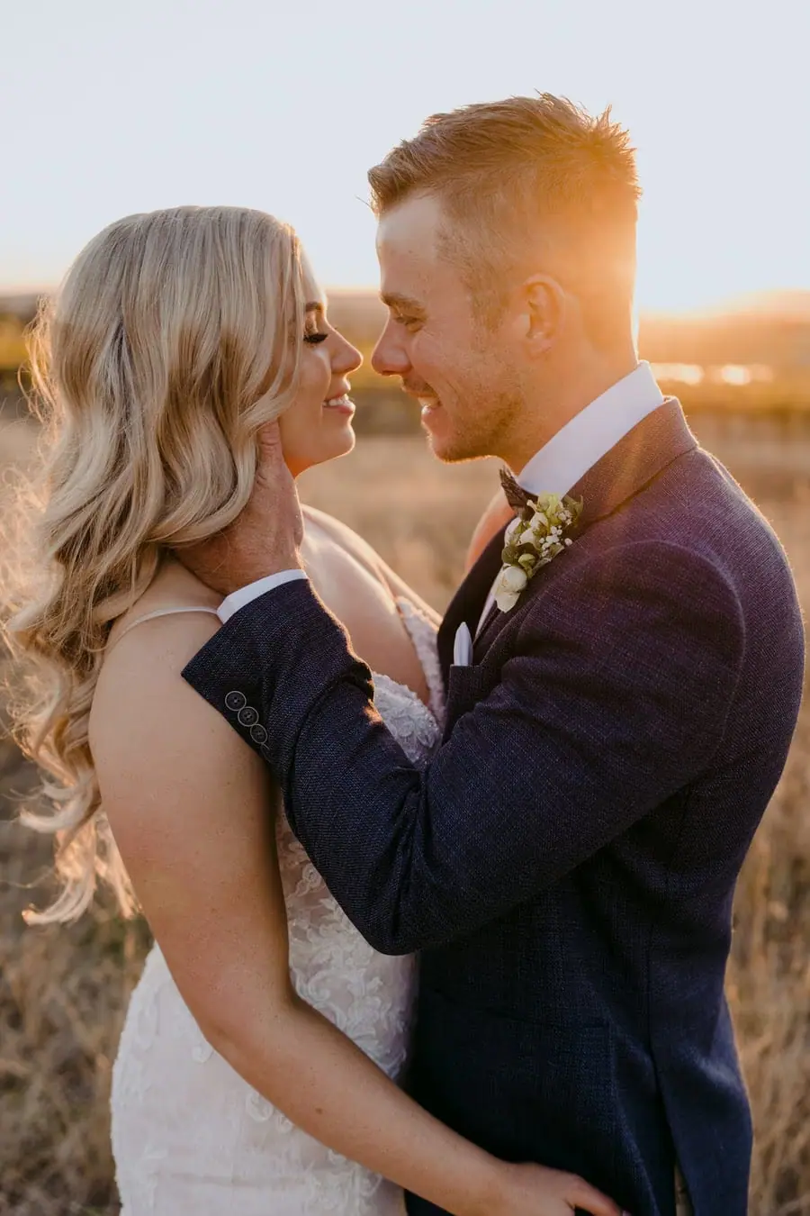Bride smiling as the groom gently holds her face at sunset