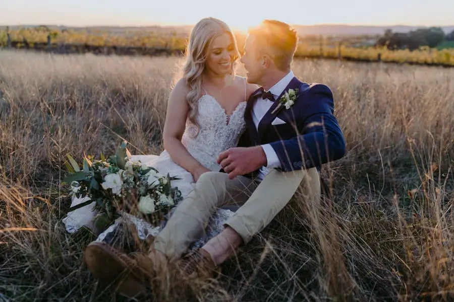 Newlyweds laughing together while seated in tall grass