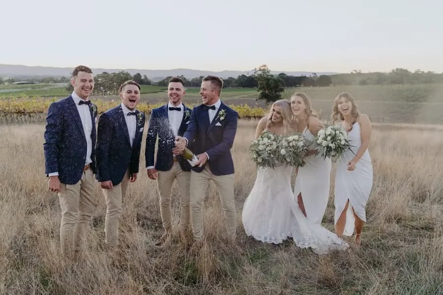 Wedding party laughing while standing in a grassy paddock
