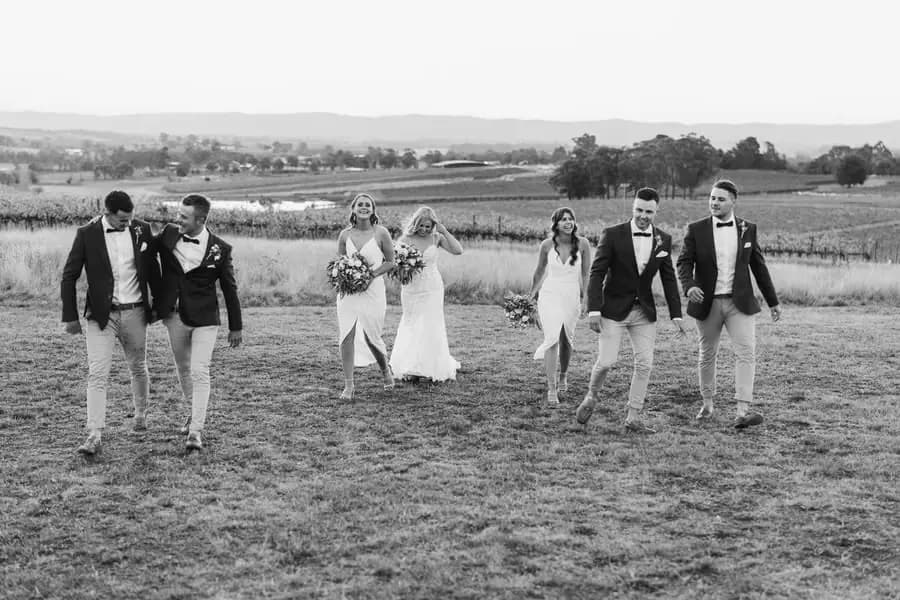Black-and-white photograph of the wedding party walking across a paddock