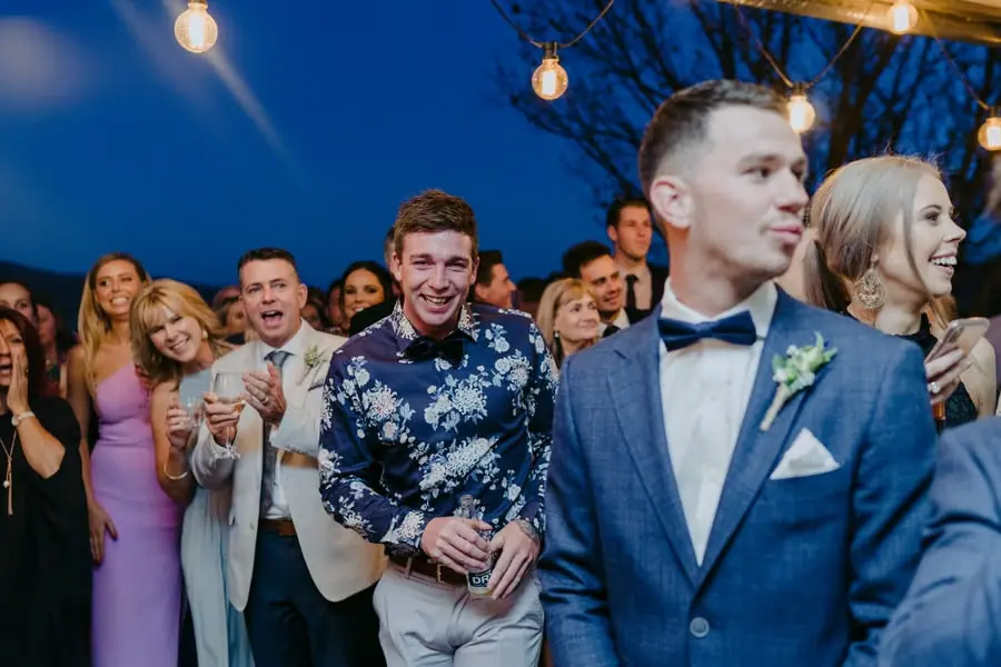 Groom looking aside as guests cheer behind him outdoors