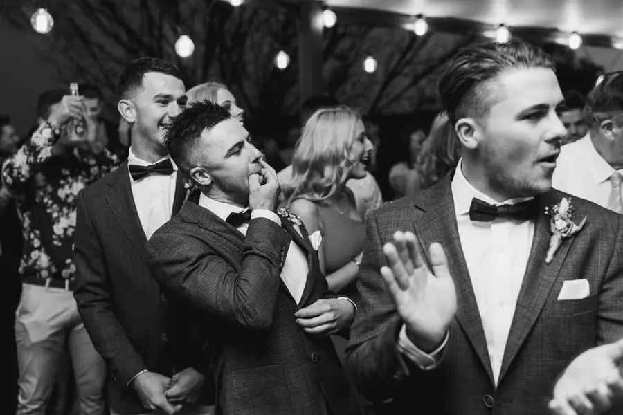 Black-and-white photograph of guests cheering beside the groom