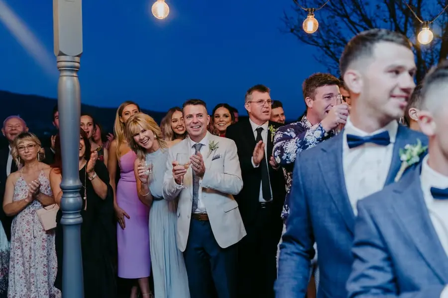Guests smiling and applauding beneath outdoor reception lights