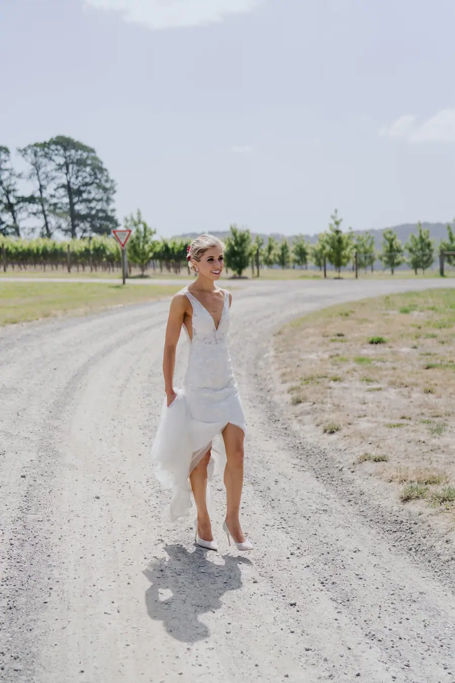 Bride walking along a gravel road beside vineyard rows
