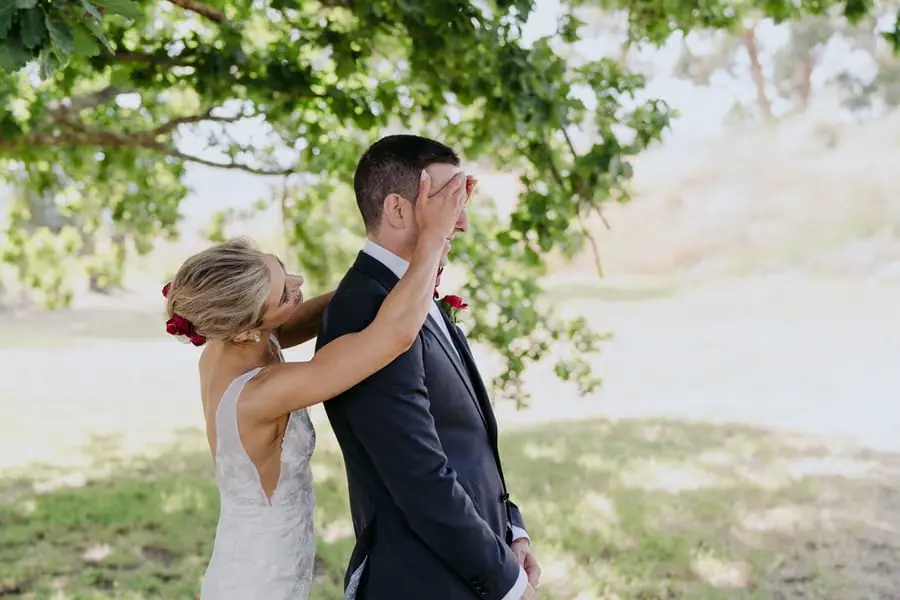 Bride covering the groom's eyes with her hands beneath a tree
