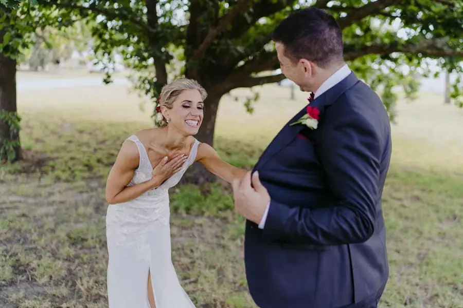 Bride laughing with one hand on her chest as the groom turns toward her