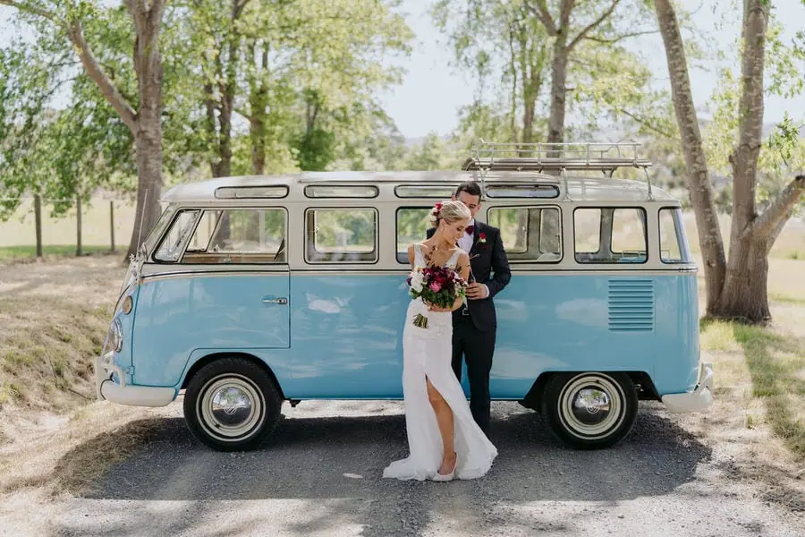Bride and groom embracing beside a blue vintage campervan