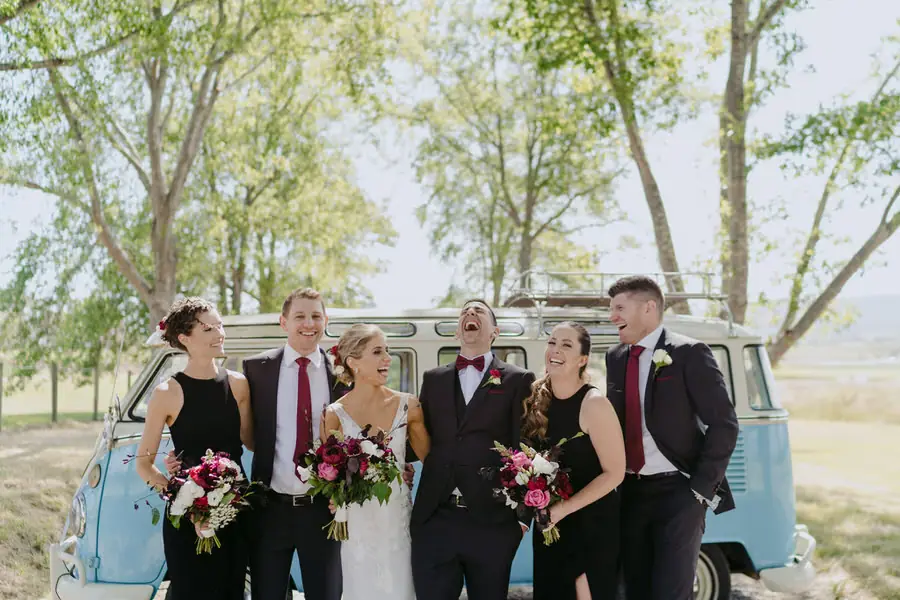Wedding party laughing together in front of a blue campervan