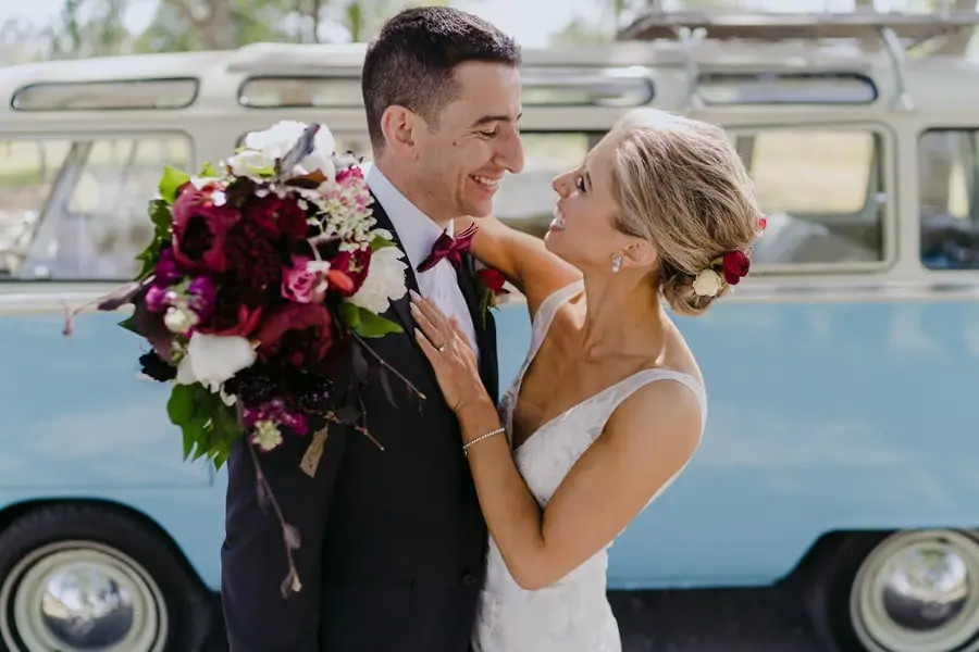 Bride smiling up at the groom with her bouquet raised beside a blue campervan