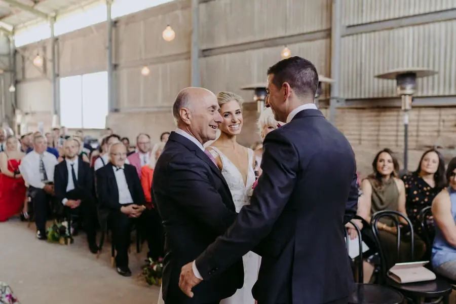 Man shaking the groom's hand as the bride stands between them at the ceremony