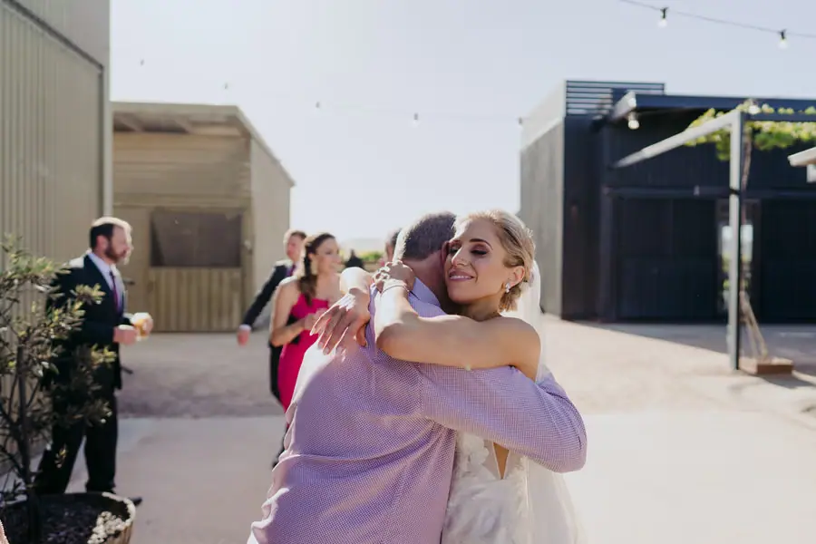 Bride embracing a guest in a lavender shirt outside the wedding venue