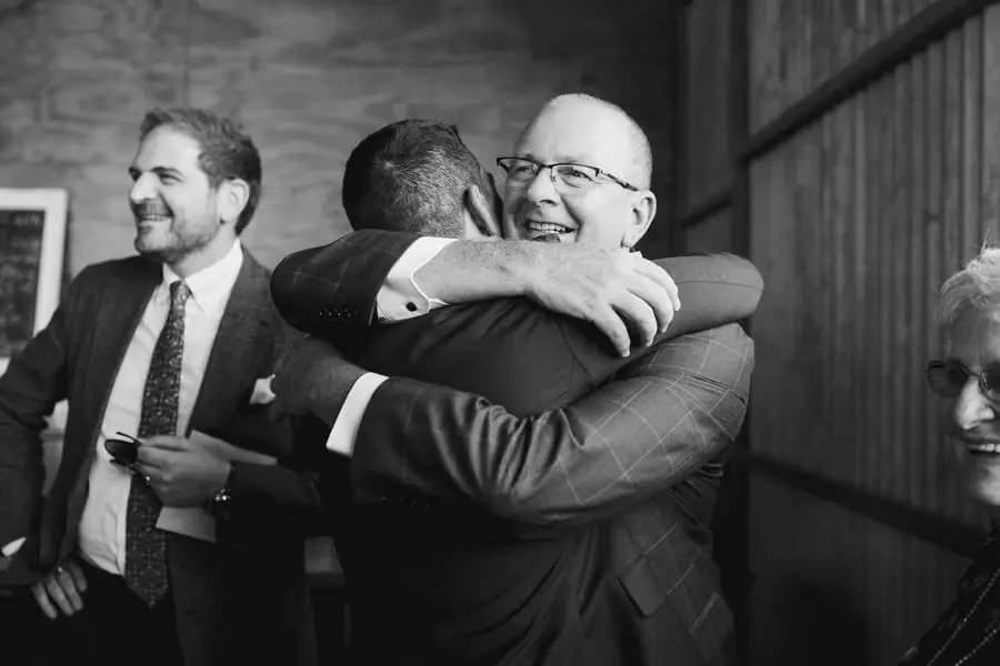 Black and white photograph of the groom hugging a smiling guest with glasses