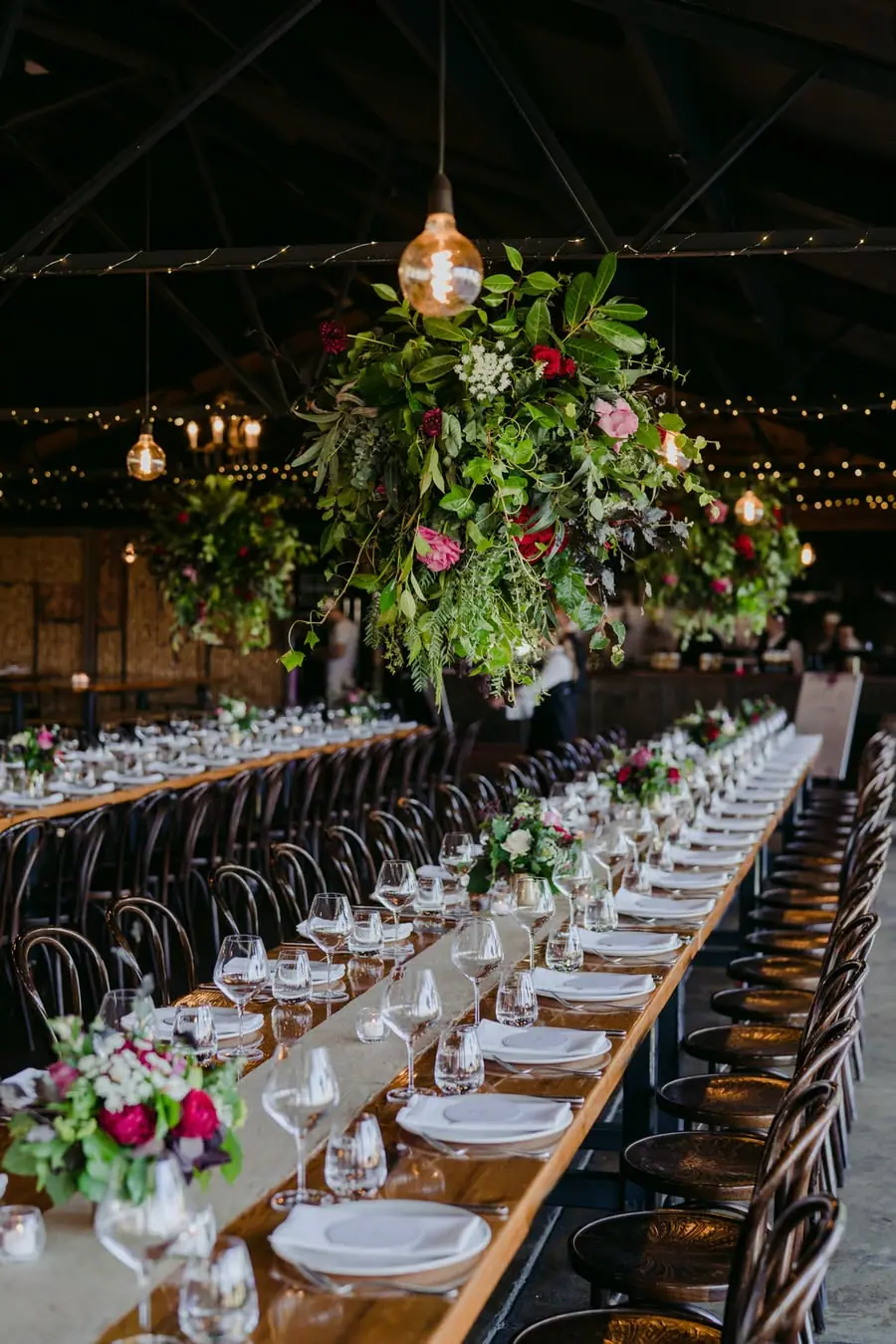 Long reception tables set with plates and glasses beneath hanging flower arrangements