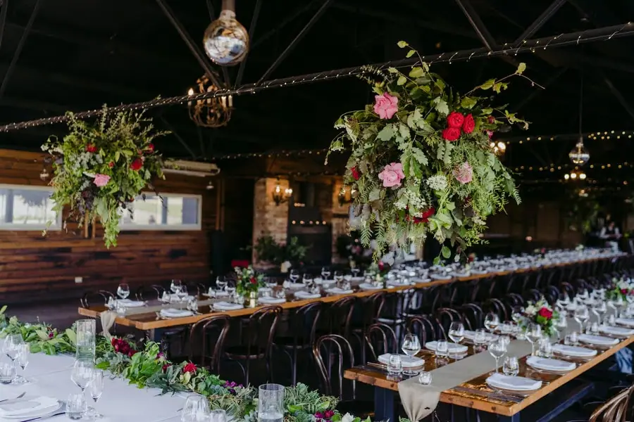 Reception tables decorated with greenery beneath a disco ball and suspended flowers