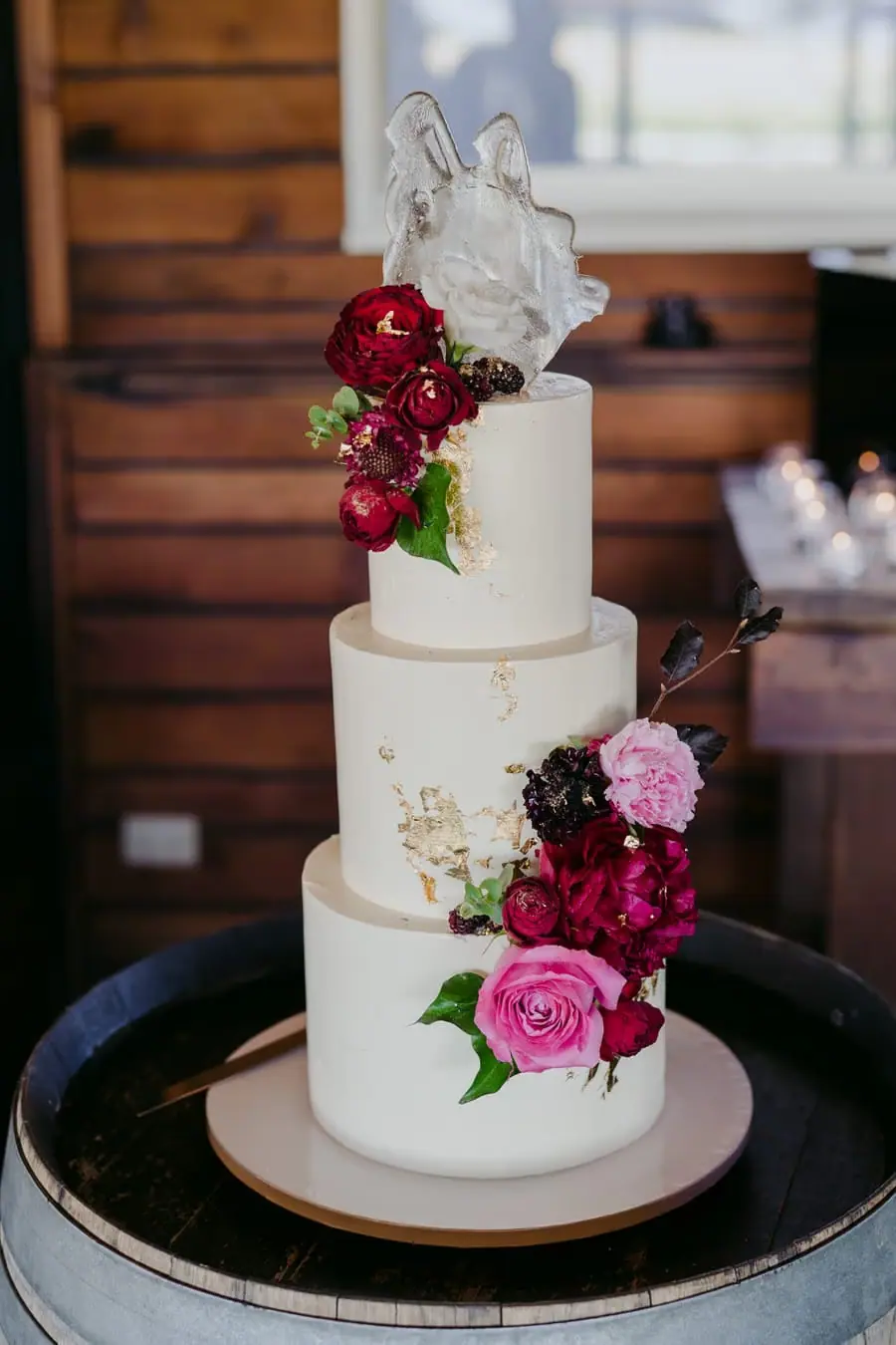 Three-tier white wedding cake decorated with burgundy and pink flowers