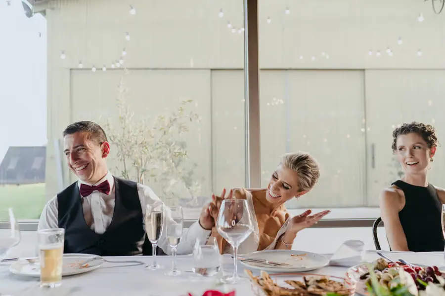 Bride and groom laughing at the reception table beside a bridesmaid
