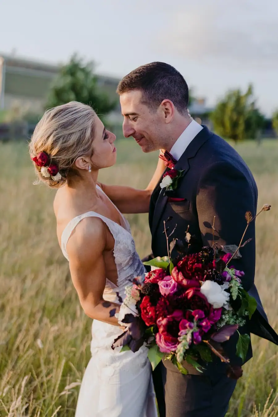 Bride and groom smiling at each other in long grass