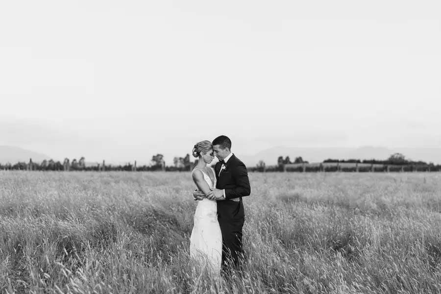 Black and white photograph of the bride and groom kissing in an open field