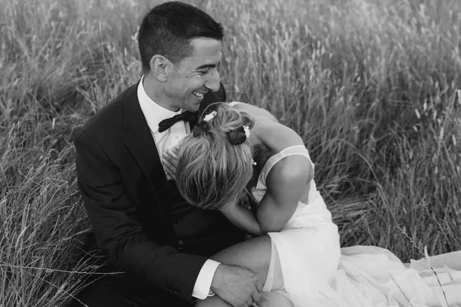 Black and white photograph of the bride resting against the groom while seated in grass