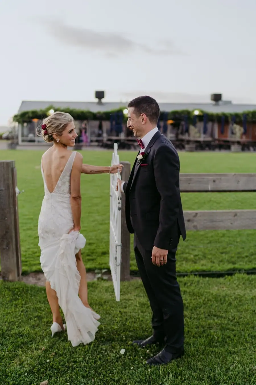 Bride and groom facing each other beside a timber fence