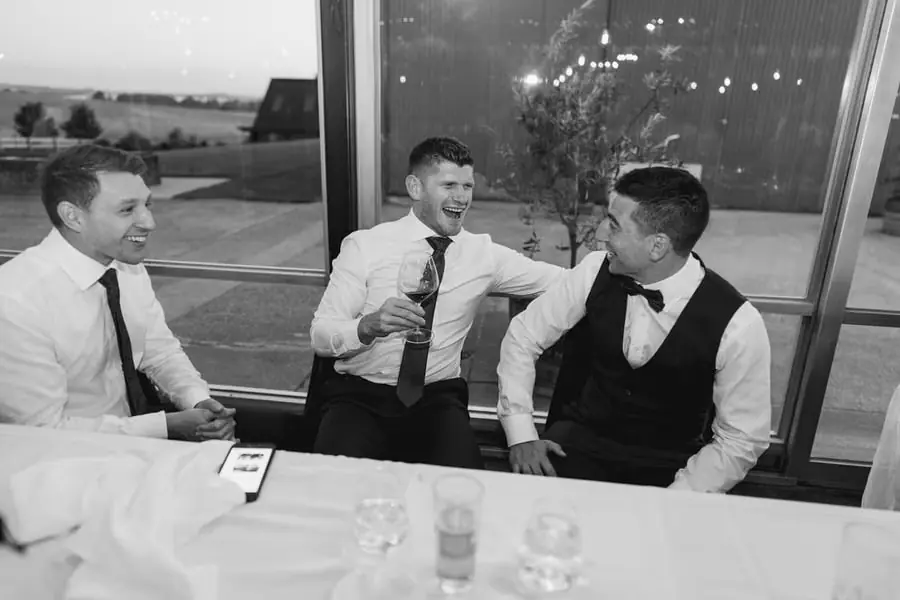 Black and white photograph of three men laughing together at the reception table