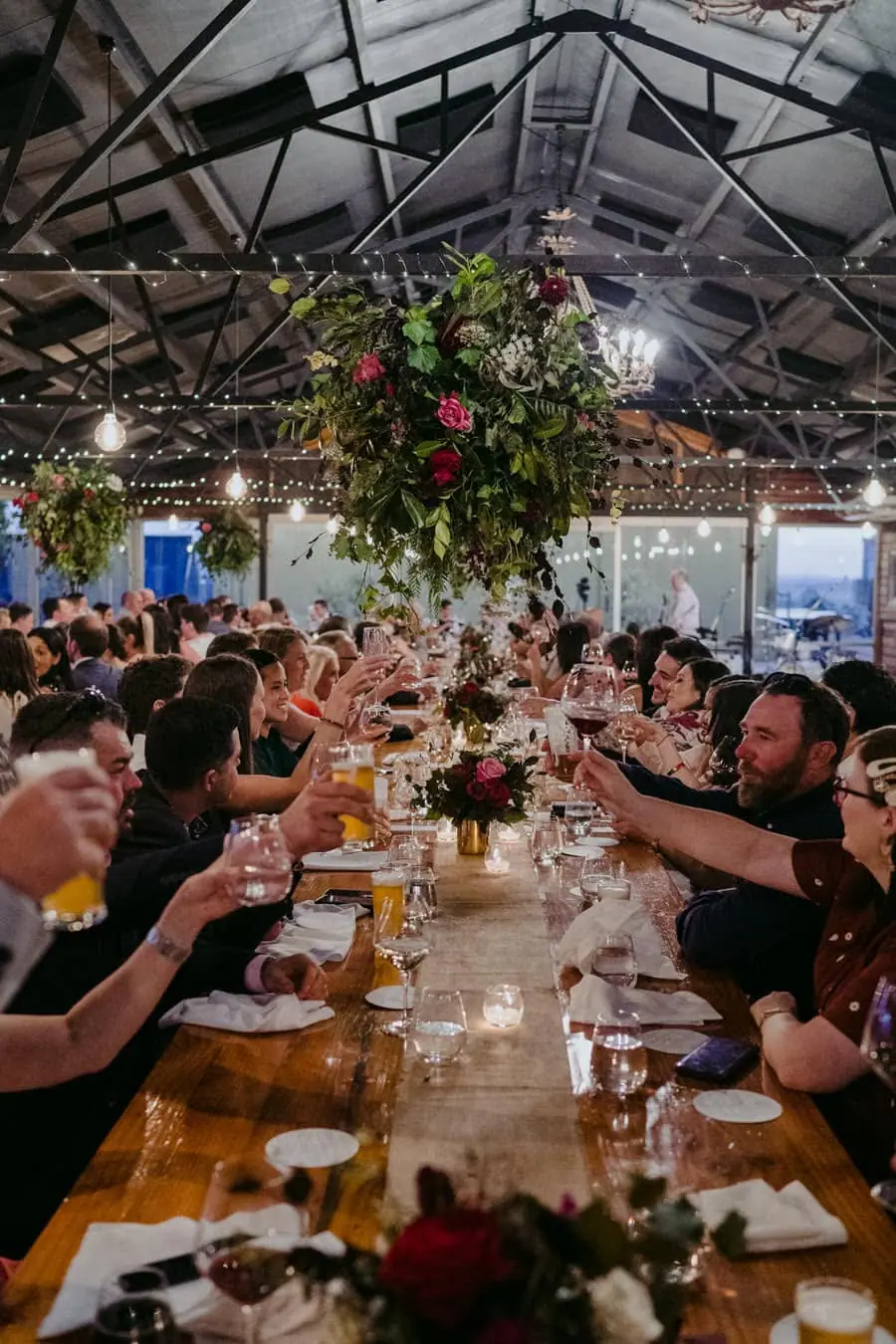 Wedding guests seated at long reception tables beneath flowers and fairy lights