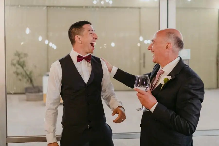 Groom laughing with a guest holding a wine glass at the reception