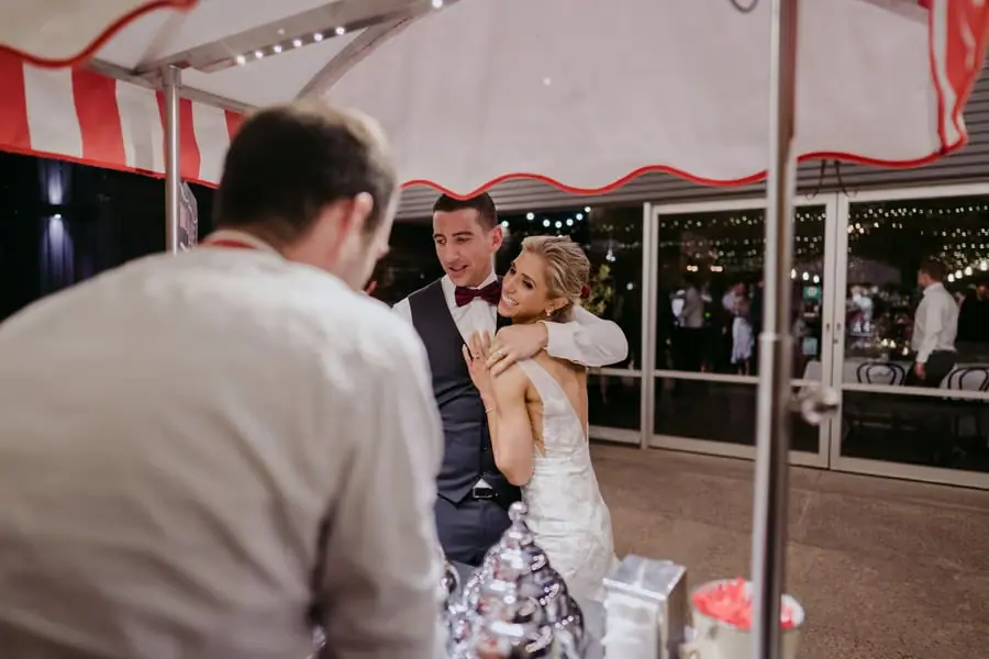 Bride and groom smiling together beside a red and white striped outdoor cart