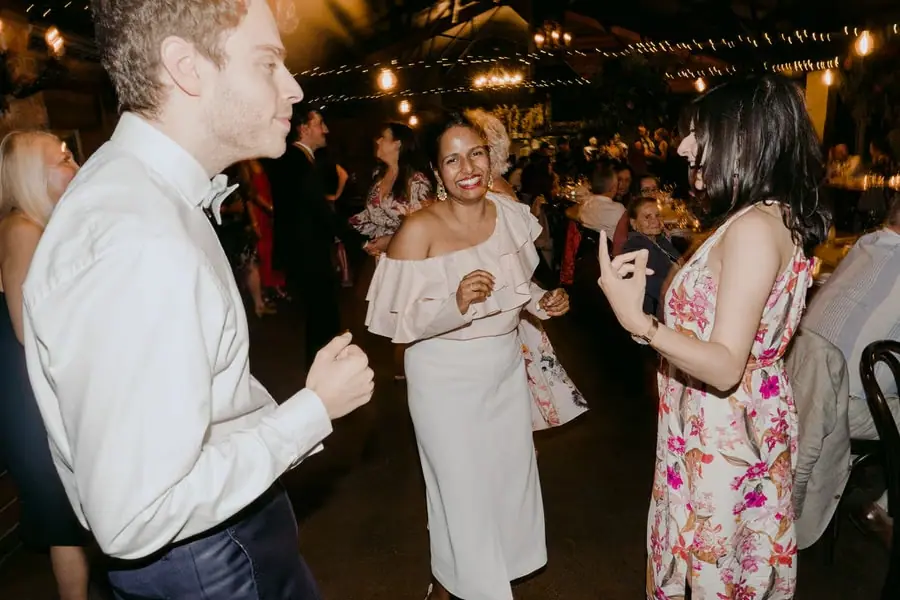 Three wedding guests dancing and laughing together at the reception