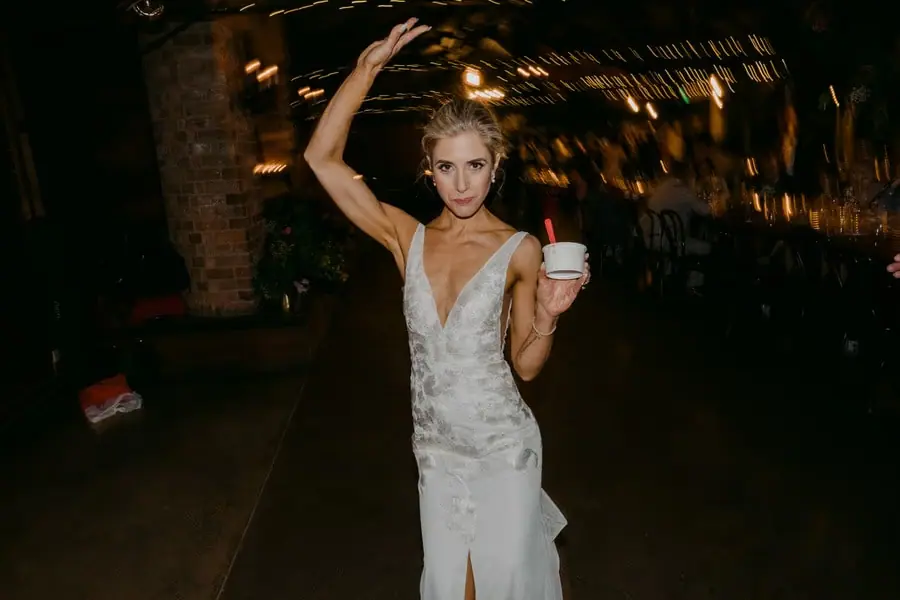 Bride dancing with one arm raised while holding a small white cup