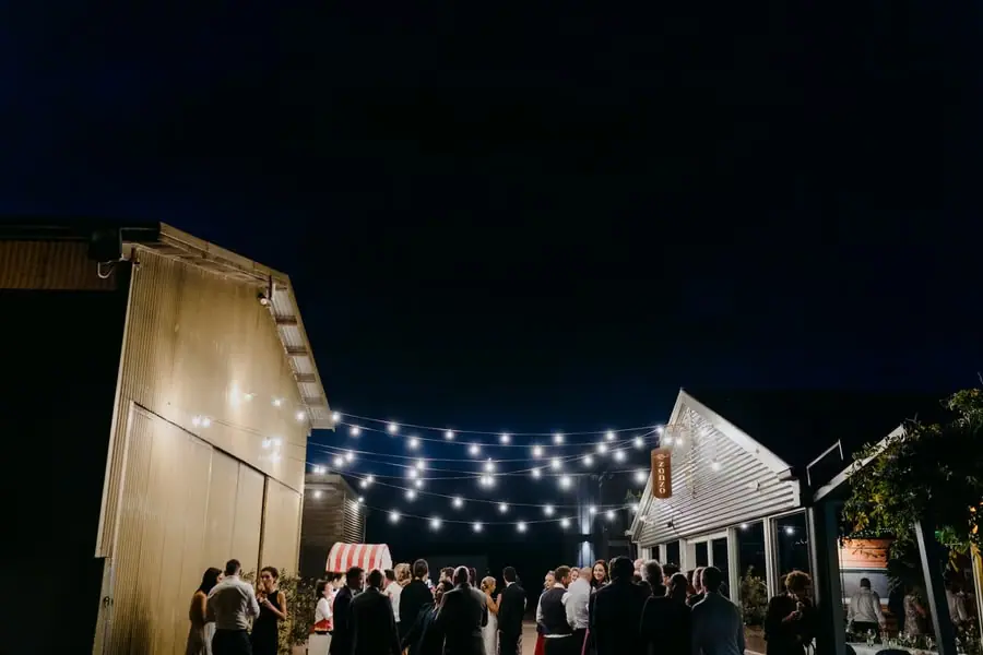 Night view of wedding guests in a courtyard beneath strings of festoon lights