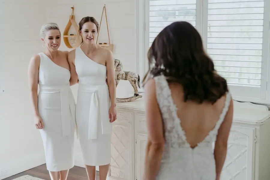 Two friends reacting as the bride approaches in her lace wedding dress