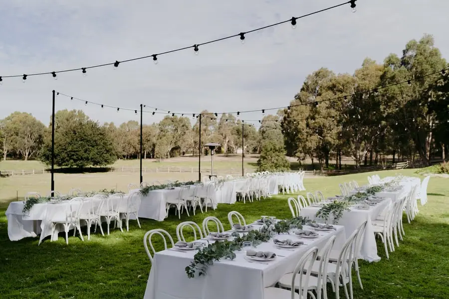 Long white-clothed reception tables arranged on a lawn beneath festoon lights
