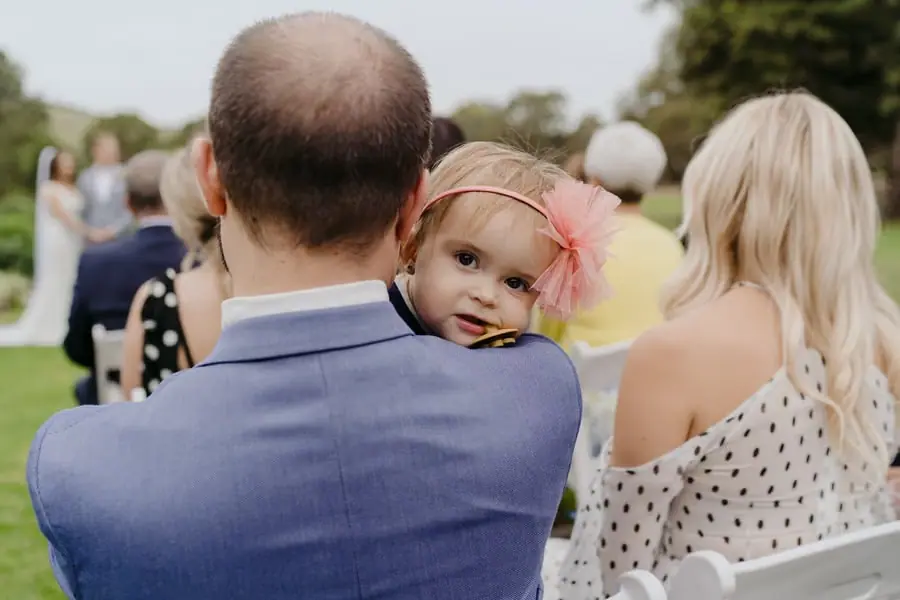 Young child peering over the shoulder of a man holding her