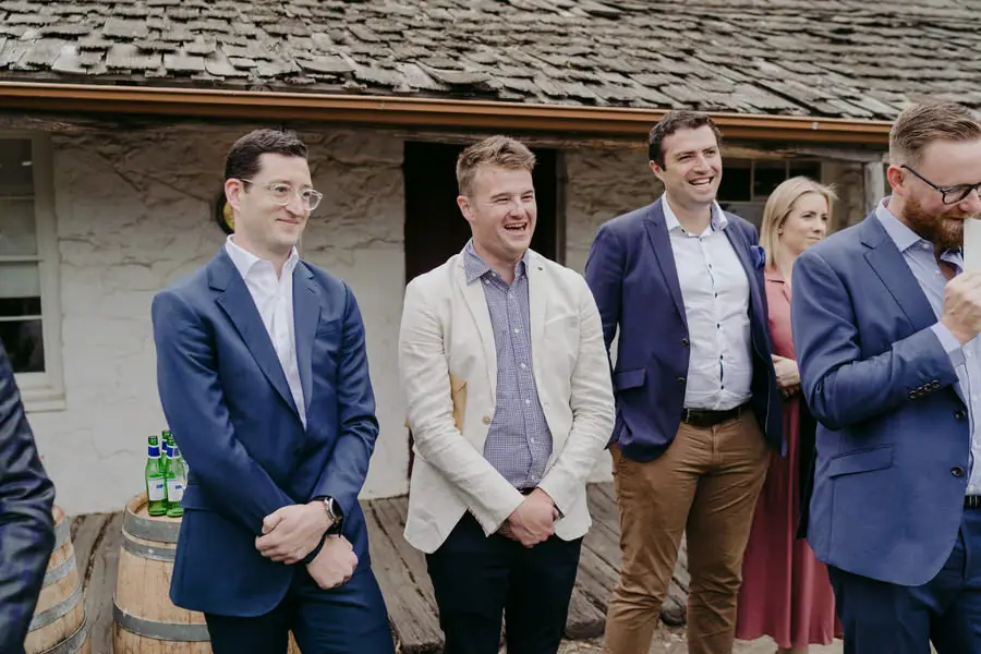 Standing guests smiling beside a rustic stone building
