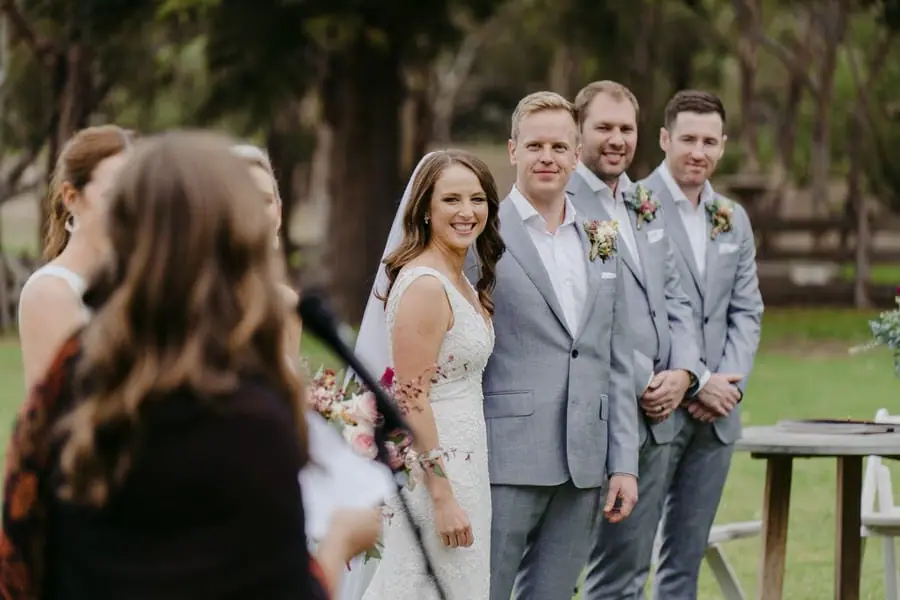 Bride and groom smiling toward the celebrant with groomsmen beside them