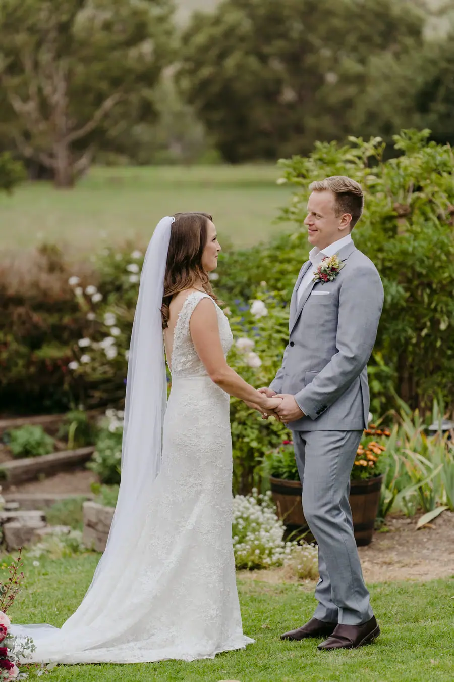Bride and groom facing one another beside garden flowers