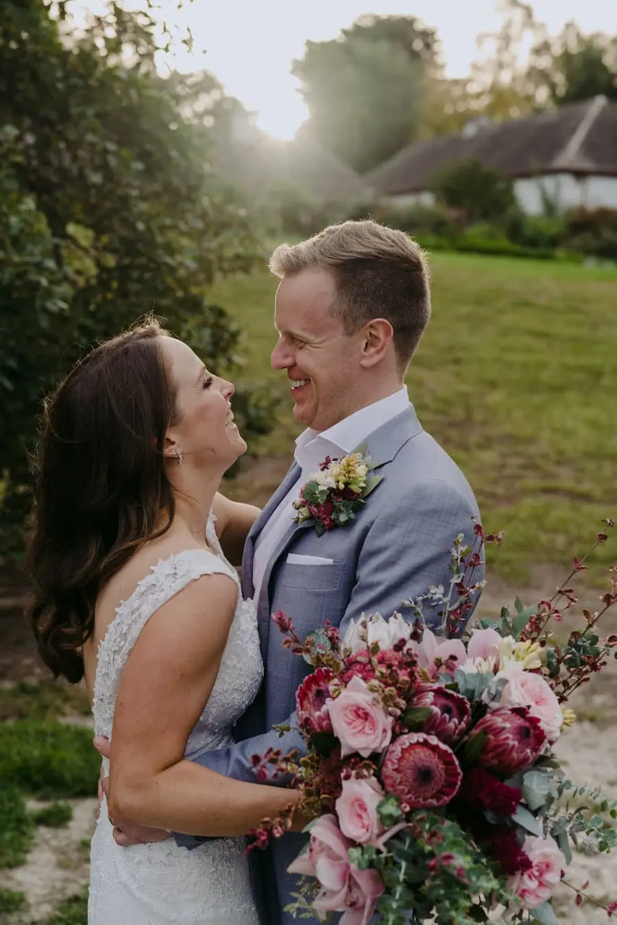 Bride and groom smiling toward one another with a bouquet between them