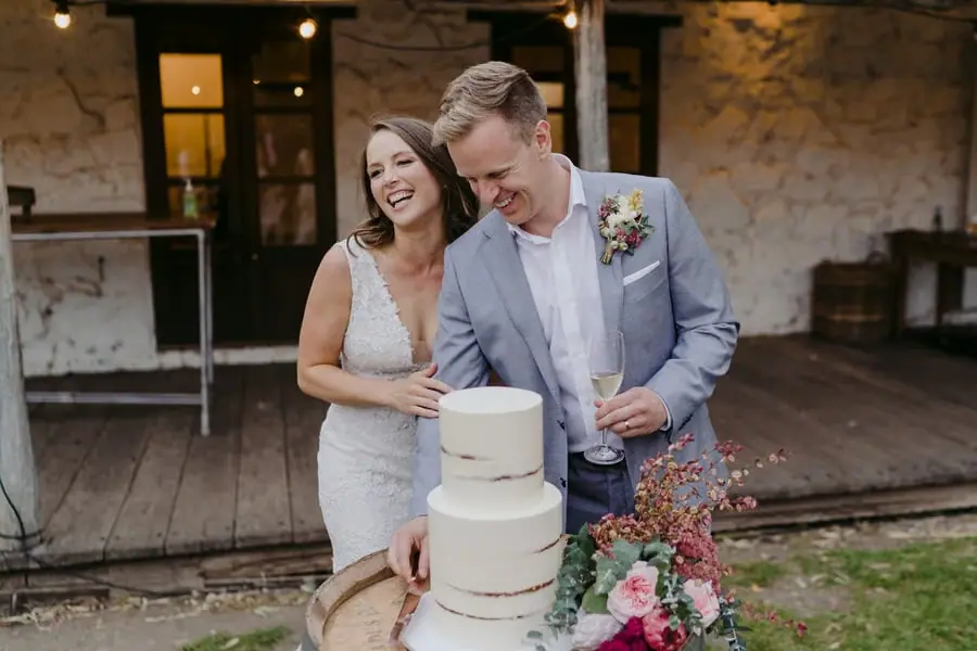 Bride and groom laughing beside a three-tier white wedding cake