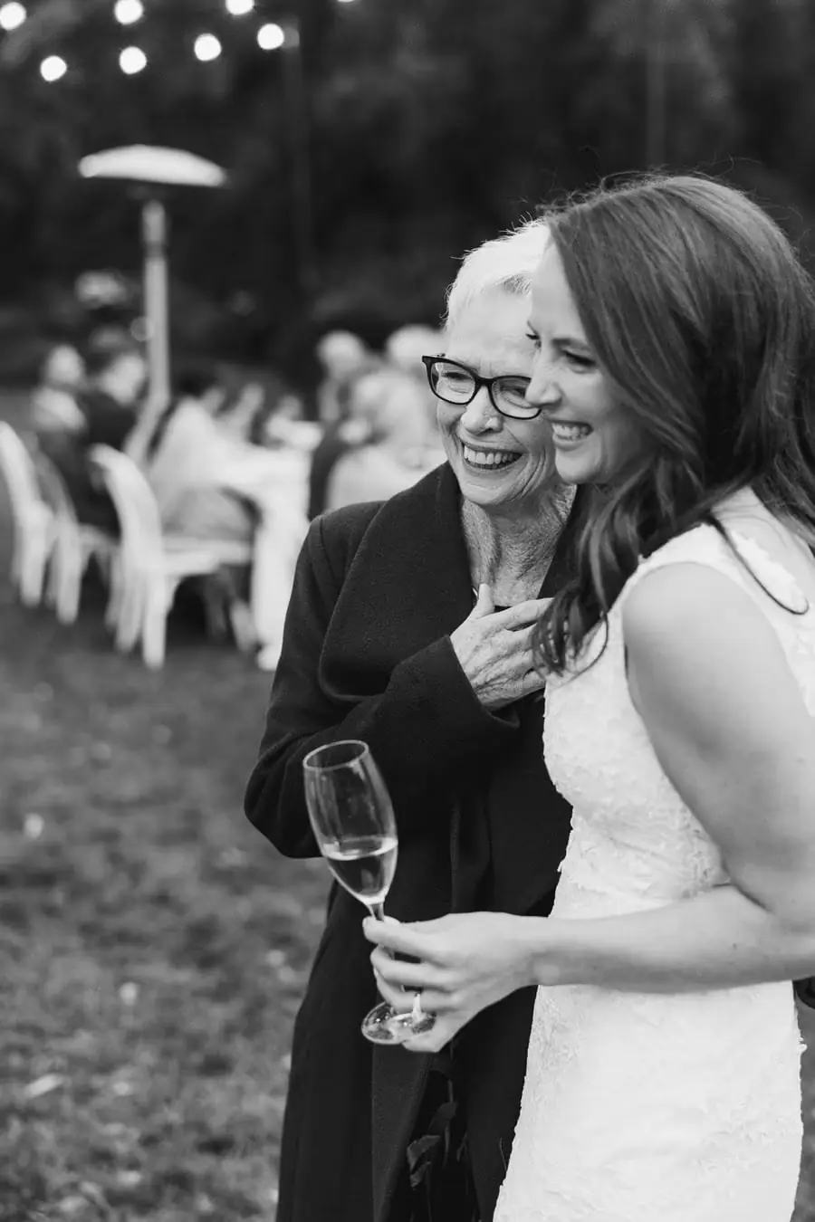 Black-and-white photograph of the bride posing closely with a guest holding a wine glass
