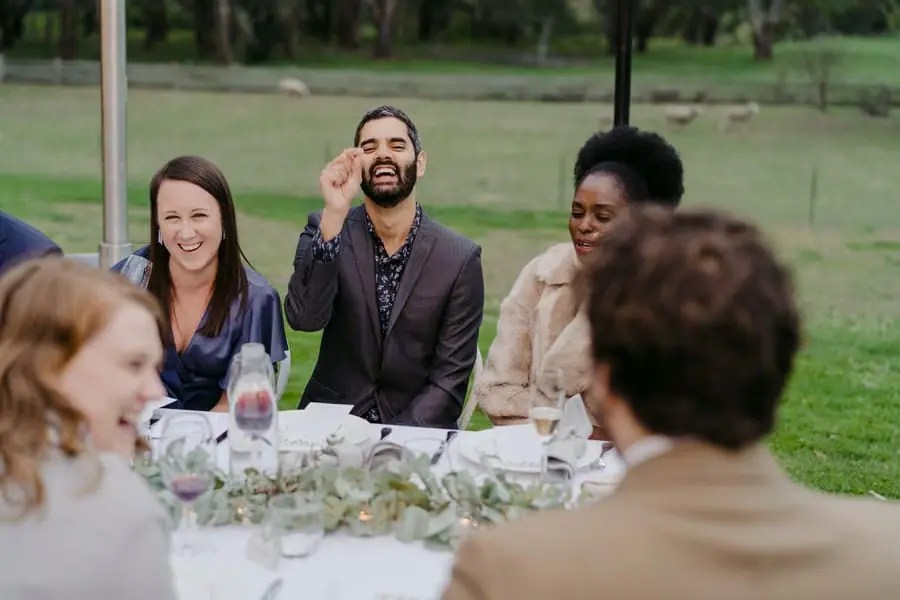 Seated wedding guests laughing together around an outdoor table