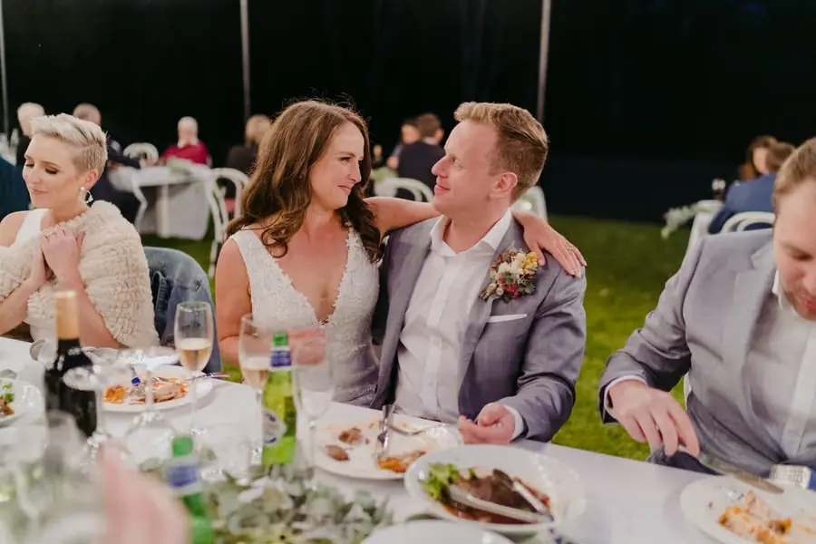 Bride and groom sitting closely together at the outdoor reception table