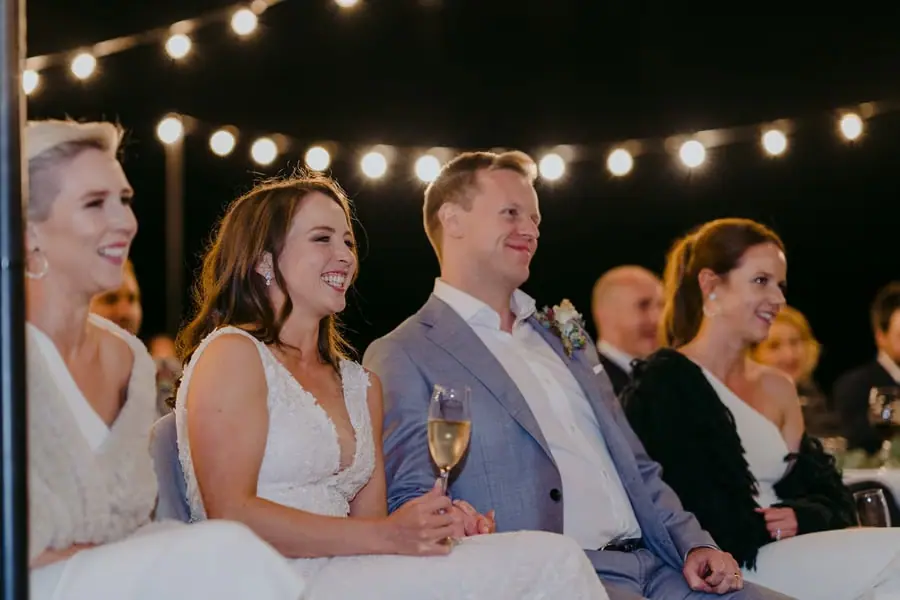 Bride and groom smiling while listening to reception speeches