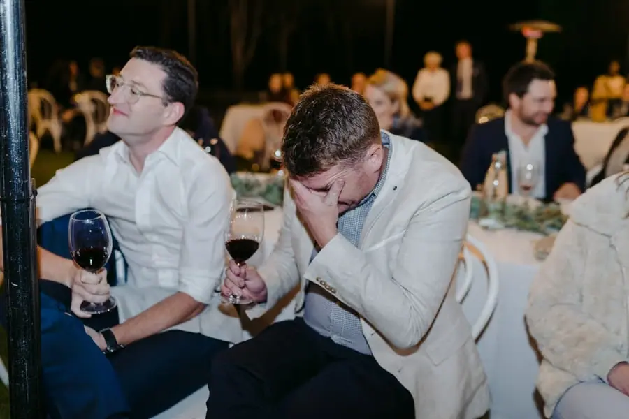 Guest covering his face while holding a glass of red wine