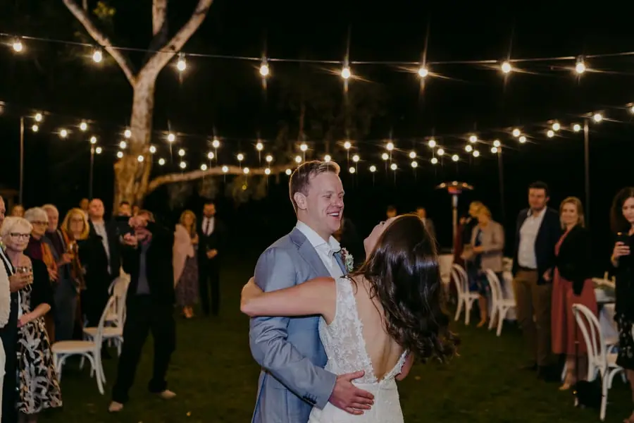 Groom dipping the bride while dancing beneath outdoor festoon lights